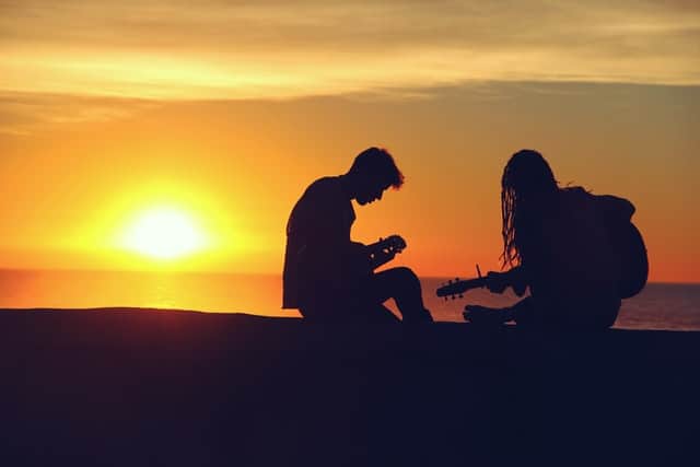 2 mensen spelen gitaar bij ondergaande zon